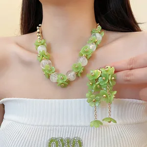 Gros plan sur un ensemble de bijoux collier floral vert et boucles d'oreilles à pompon