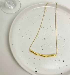 Detail of minimalist gold plated stainless steel curved bar pendant necklace on a plate