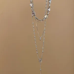 Macro view of a four-layer silver layered necklace with teardrop and medal pendants.