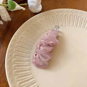 Primo piano di un elegante fermaglio per capelli in chiffon rosa su piatto crema.