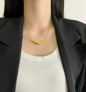 Detailed close-up of a minimalist gold curved pendant necklace worn on a black blazer