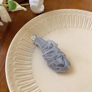 Primo piano di un'elegante molletta per capelli in chiffon plissettato blu-grigio su un piatto.