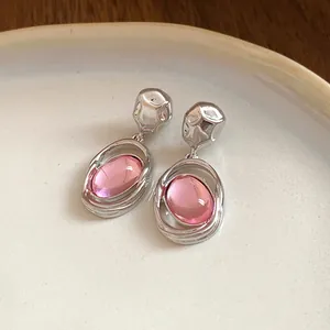 Close-up shot of elegant retro pink acrylic oval pendant earrings resting on a white ceramic plate