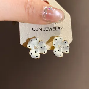 Detail view of white enamel flower stud earrings with black polka dots and pearl