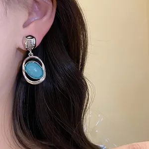 Close-up detail of retro silver dangle earring with teal acrylic oval stone on ear
