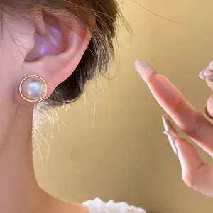 Detailed macro shot of vintage pearl and cat's eye stud earrings on ear.