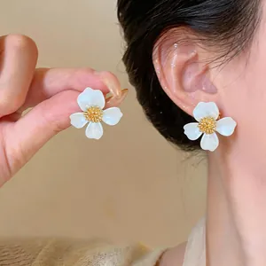 Primo piano dettagliato di un orecchino a fiore in smalto bianco con stame dorato su modella