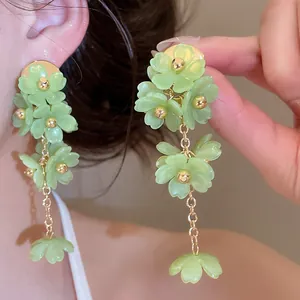 Détail en gros plan d'élégantes boucles d'oreilles à fleurs vert clair et accents dorés