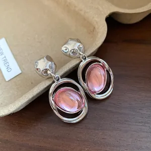 Close-up of vintage silver oval pendant earrings with pink acrylic stones on wood.