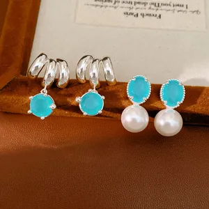 Close-up of elegant turquoise zircon and white pearl drop earrings on a brown surface