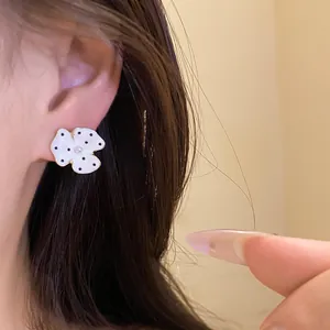 Detailed view of a white polka dot flower earring with pearl center worn on an ear.