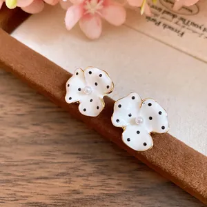 Close-up detail of white polka dot flower earrings with pearl centers and gold trim.