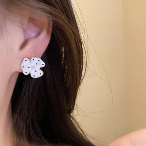 Detail of white flower enamel stud earring with black polka dots and pearl worn on the ear.