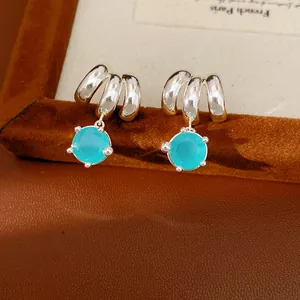 Detailed close-up of geometric silver earrings with bright blue round zircon stones