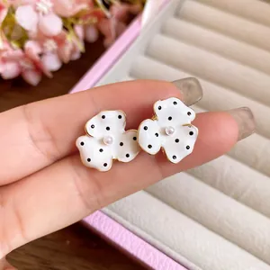 Macro view of white enamel flower stud earrings with black polka dots and a center pearl