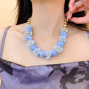 Gros plan d'un collier floral bleu clair avec perles dorées porté par un modèle