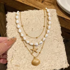 Collier doré multi-rangs avec pendentifs étoile de mer et conque sur fond texturé