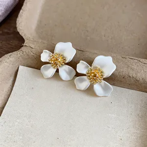 Eleganti orecchini a lobo a fiore in smalto bianco con centro dorato su sfondo beige