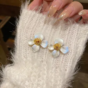 Macro dettaglio di orecchini a lobo minimalisti a forma di fiore su maglione morbido