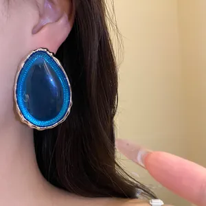 Detailed close-up view of a blue teardrop resin stud earring worn on a model's ear