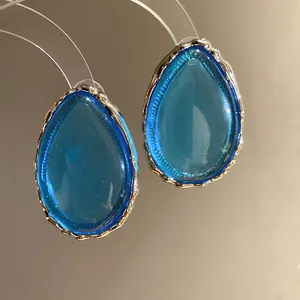 Close-up of elegant blue teardrop resin earrings with textured gold-tone metallic edges.