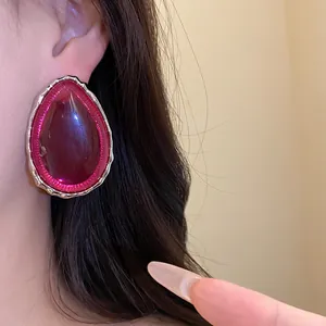 Close-up of large magenta resin teardrop earring with silver wavy border on model