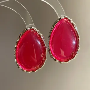 Close-up detail of teardrop-shaped pink resin stud earrings with elegant wavy gold edges