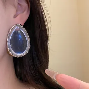 Close-up detail of a large teardrop resin earring with a silver textured frame on ear.