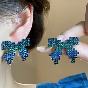 Close-up detail of stylish pixelated bow stud earrings with blue and green crystals