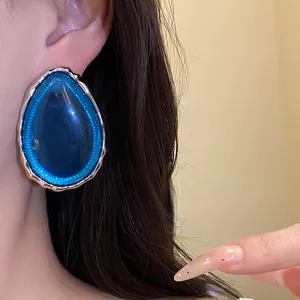 Close-up view of a vintage blue resin teardrop earring with wavy gold-tone trim on model