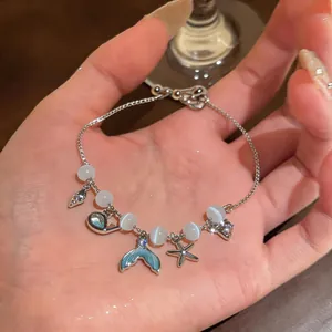Close-up detail of an ocean-themed charm bracelet with mermaid tail and cat-eye stones