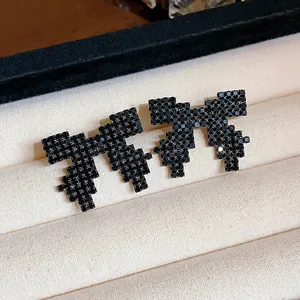Detailed view of black pixelated bow earrings with shiny rhinestones in a display box.