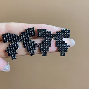 Close-up macro view of pixelated black rhinestone bow stud earrings with silver needle base