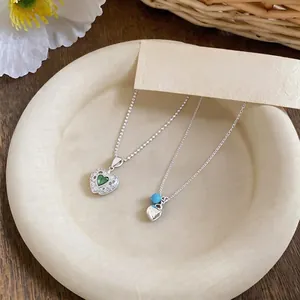 Silver necklace with green zircon apple and blue heart pendants on a neutral tray background.
