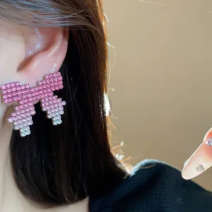 Close-up detail view of a pink gradient pixel-art bow earring adorned with shiny rhinestones.