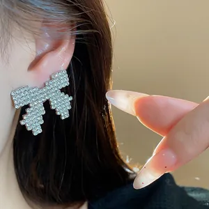Close-up detail of an elegant rhinestone-encrusted silver needle bow stud earring on ear