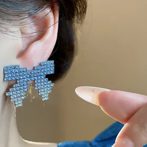 Close-up macro detail of pixel bow stud earrings with blue gradient rhinestone inlay