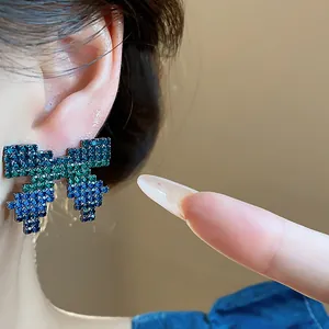 Detail view of pixelated bow stud earring featuring blue and green stones worn on the ear.