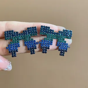 Detailed view of pixelated bow stud earrings featuring vibrant blue and green pavé rhinestones