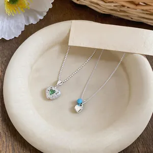 Close-up of minimalist silver necklaces with heart pendant and green zircon gemstone detail