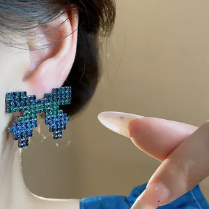 Close-up view of pixel art bow earrings with blue and green crystals worn on ear