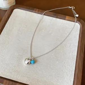 Close-up of minimalist silver heart necklace with a small turquoise bead on wooden tray