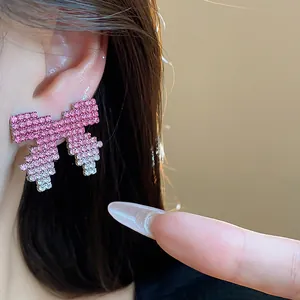 Close-up view of pixel art bow stud earrings with pink gradient rhinestones worn on the ear.