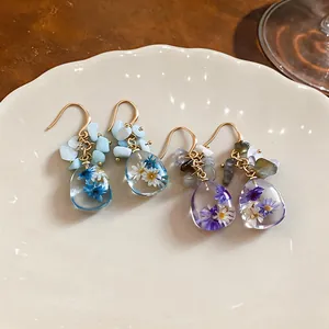 Handmade resin earrings with real dried flowers and stone beads on a cream plate