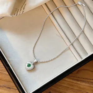 Silver apple pendant with green zircon gemstone displayed in a cream jewelry organizer.