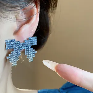 Close-up of a pixelated bow earring featuring blue and white gradient rhinestones
