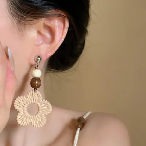Close-up detail of bohemian flower rattan woven earrings with decorative wood beads.