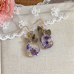 Detailed view of gold-tone drop earrings featuring purple dried flowers in clear resin.