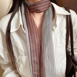 Detailed view of an elegant striped mesh scarf worn with a white linen shirt