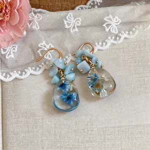 Close-up detail of resin teardrop earrings with preserved blue and white dried flowers.